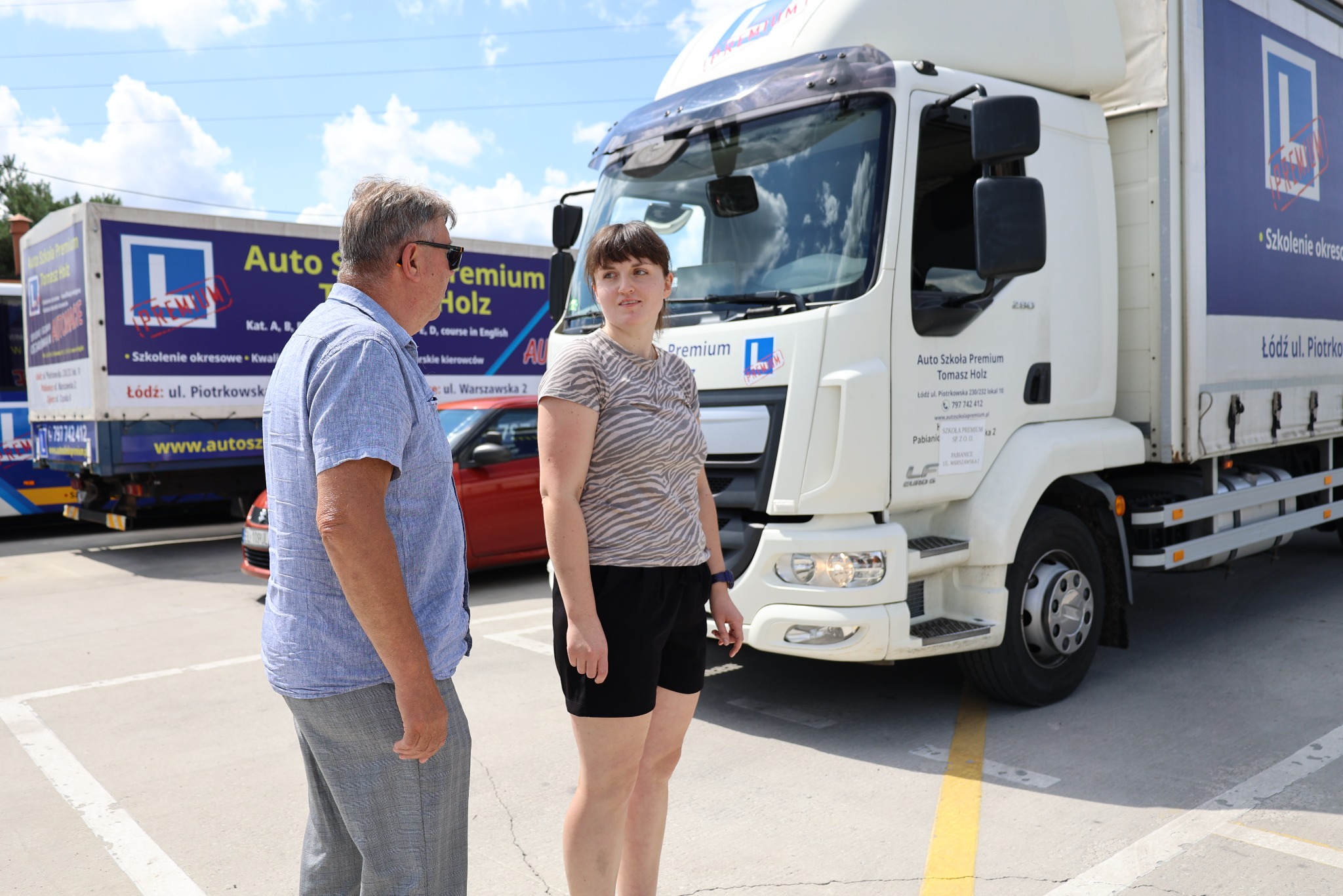 Instruktorzy auto szkoły Premium Tomasz Holz rozmawiają na tle ciężarówki z logo szkoły w Łodzi. Szkolenia okresowe i kwalifikacje kierowców.