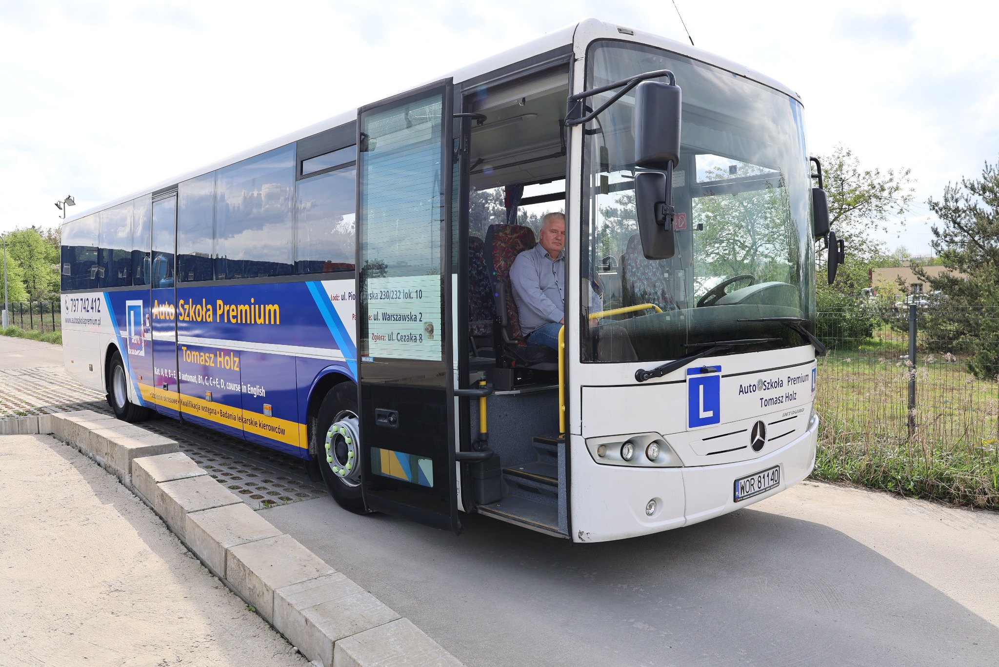 Autobus Auto Szkoły Premium z otwartymi drzwiami, widoczny instruktor za kierownicą. Tablica z literą 'L' na przodzie pojazdu.