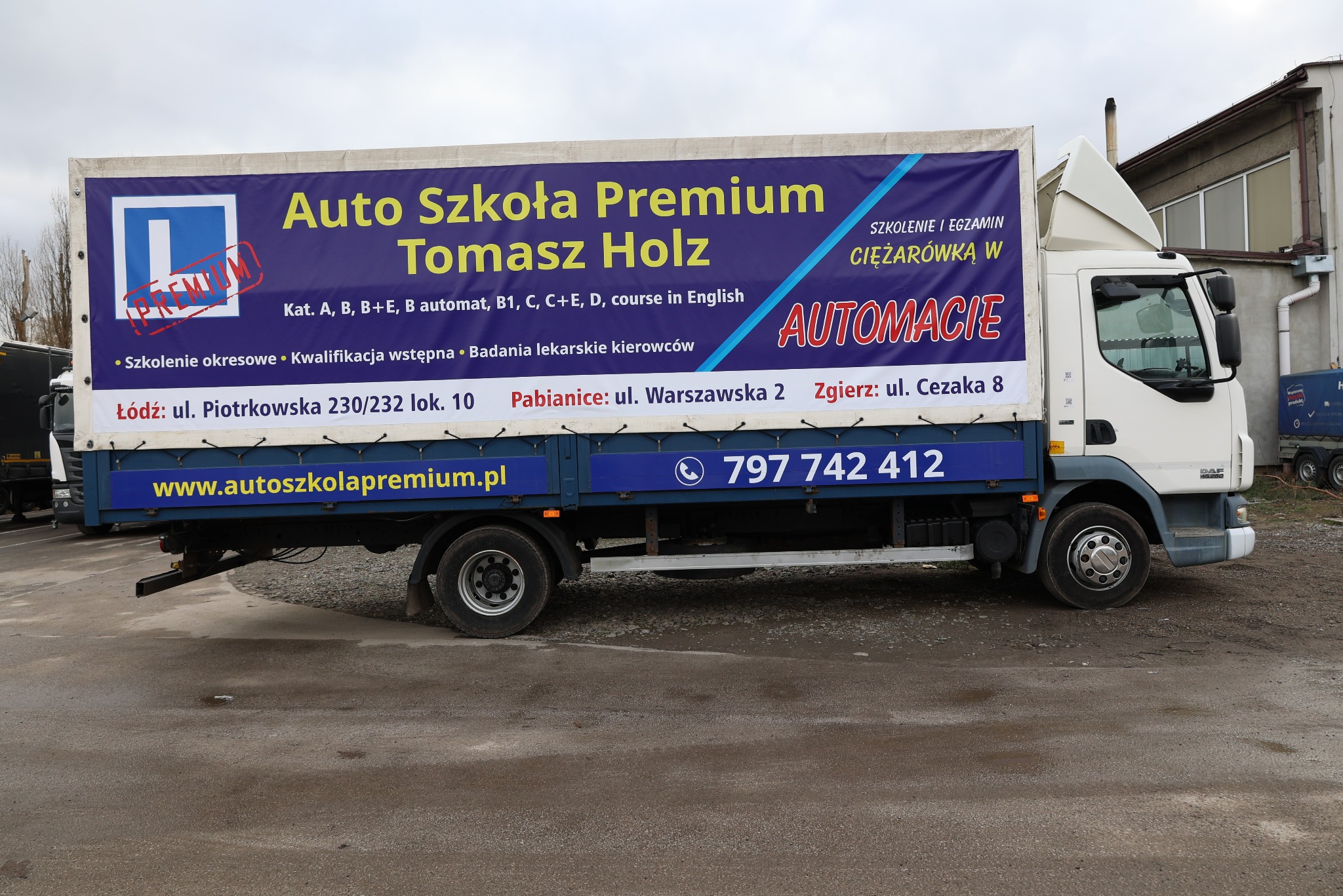 Ciężarówka z reklamą Auto Szkoły Premium Tomasz Holz, oferującej kursy na kat. A, B, C i inne, z oddziałami w Łodzi, Pabianicach i Zgierzu. Numer telefonu widoczny.