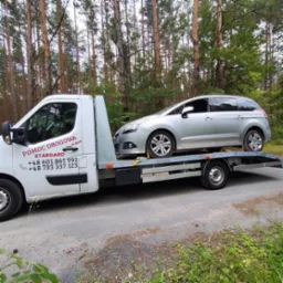 Laweta Pomocy Drogowej Stargard z srebrnym autem osobowym na platformie, na tle leśnym. Widoczne numery kontaktowe na pojeździe.