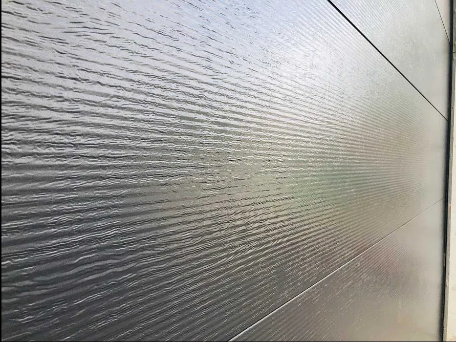 Szara brama segmentowa z poziomym wzorem przypominającym fale, widziana pod kątem z bliska, ukazująca fakturę i detale paneli.