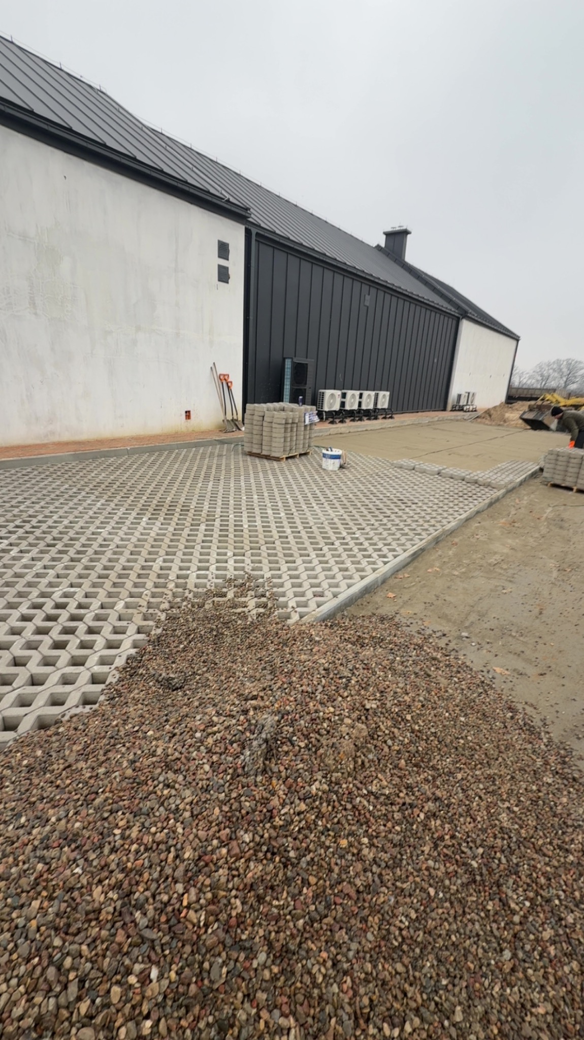 Układanie ażurowych płyt i wypełnianie ich kamieniem w Kwilcz. Widoczne narzędzia i materiały budowlane. Częściowo ułożona nawierzchnia na tle budynku.