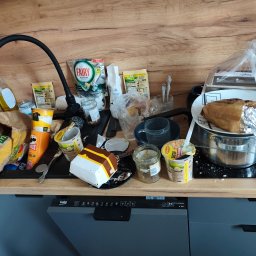 Anton Suvorov - Zabrudzony blat kuchenny z resztkami jedzenia, opakowaniami po posiłkach, brudnymi naczyniami i środkami czystości. Widoczna zmywarka Beko.