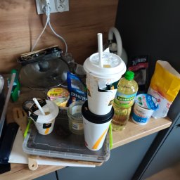 Anton Suvorov - Niezorganizowany blat kuchenny z resztkami jedzenia, kubkami po napojach, olejem Kujawski i produktami spożywczymi, ukazujący potrzebę sprzątania i ogarnięcia przestrzeni.