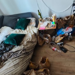 Anton Suvorov - Zaniedbane wnętrze pokoju: rozrzucone śmieci, puste torby po jedzeniu, butelka po winie i niepościelone łóżko z zielonymi poduszkami.