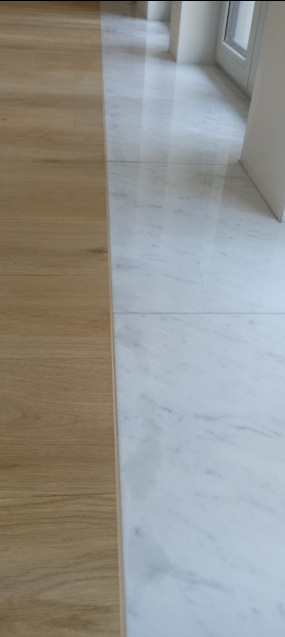 Połączenie jasnych paneli podłogowych i białych płytek marmurowych. Widok na podłogę wzdłuż okna. Kontrast materiałów i kolorów, nowoczesny design.