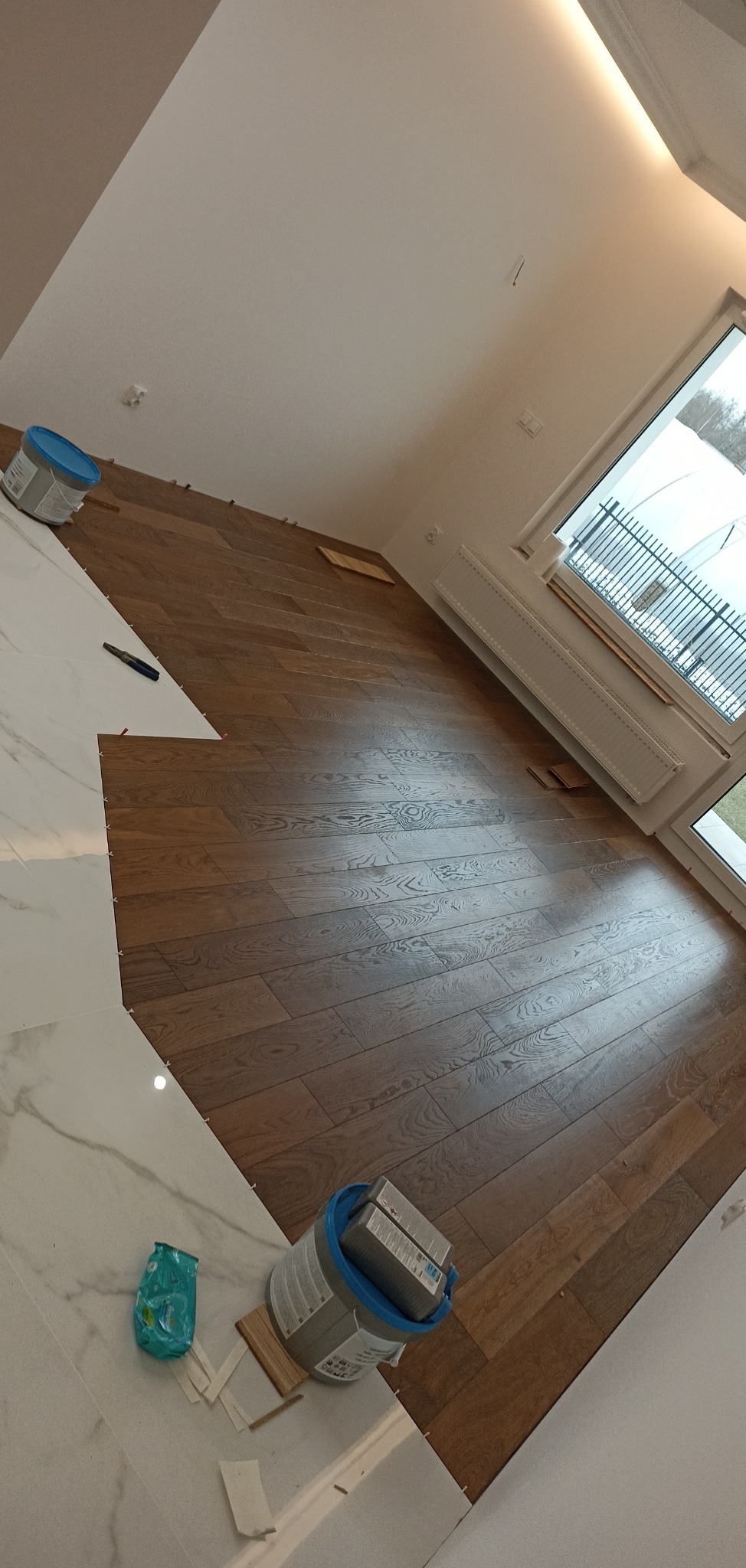 Układanie paneli podłogowych w Zabrodziu, widoczne narzędzia i fragment ułożonej podłogi z płytek imitujących marmur. Etap prac wykończeniowych.