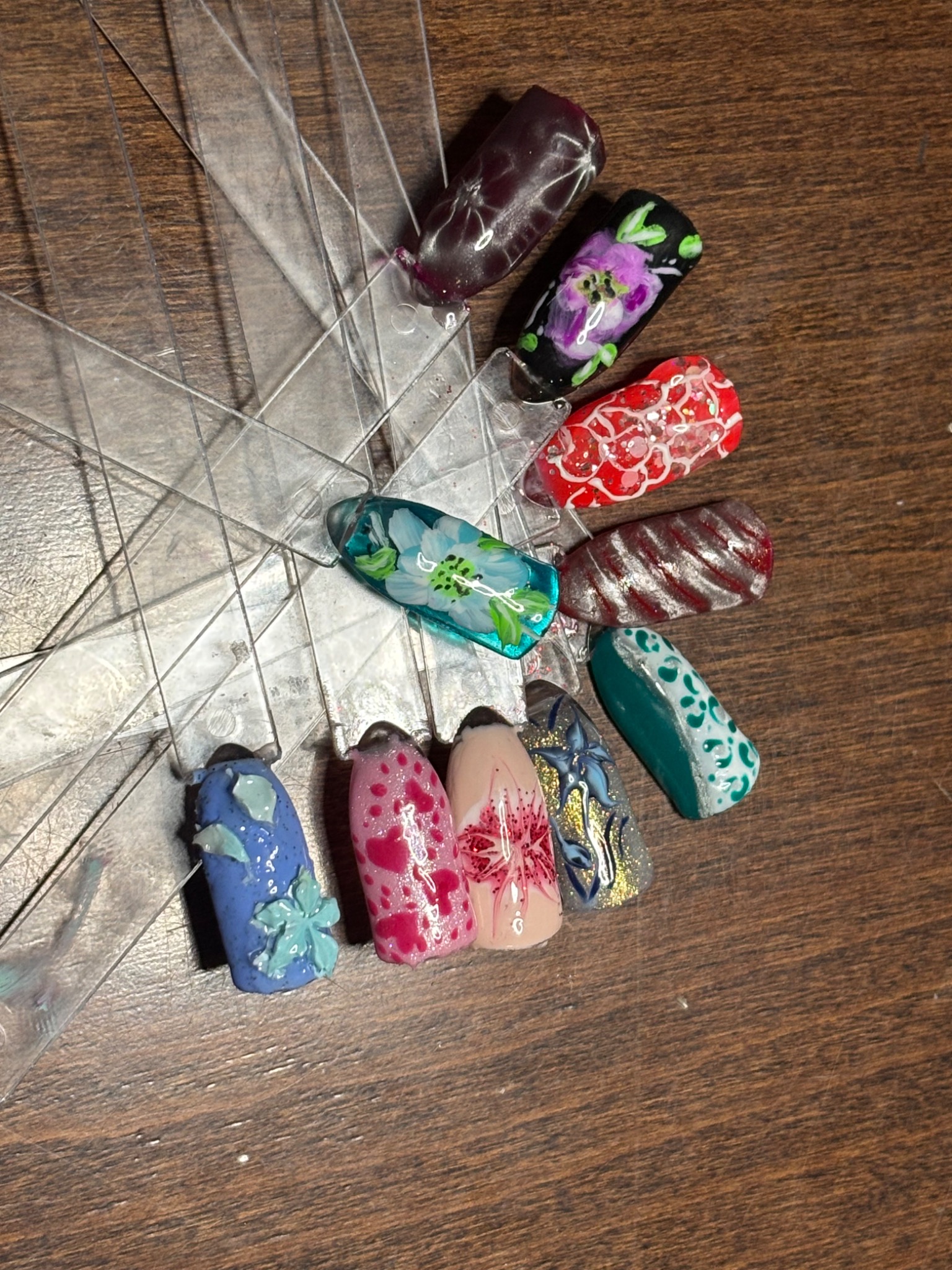 Paleta z wzorami zdobień paznokci: kwiaty, brokat, ombre. Różne kolory i style na przezroczystych wzornikach, prezentacja technik manicure.