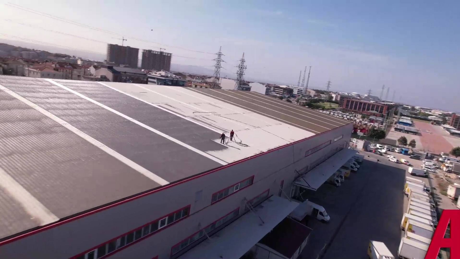 Dwóch robotników czyści dach przemysłowy za pomocą węży ciśnieniowych na tle zabudowy miejskiej i błękitnego nieba. Praca na wysokościach.