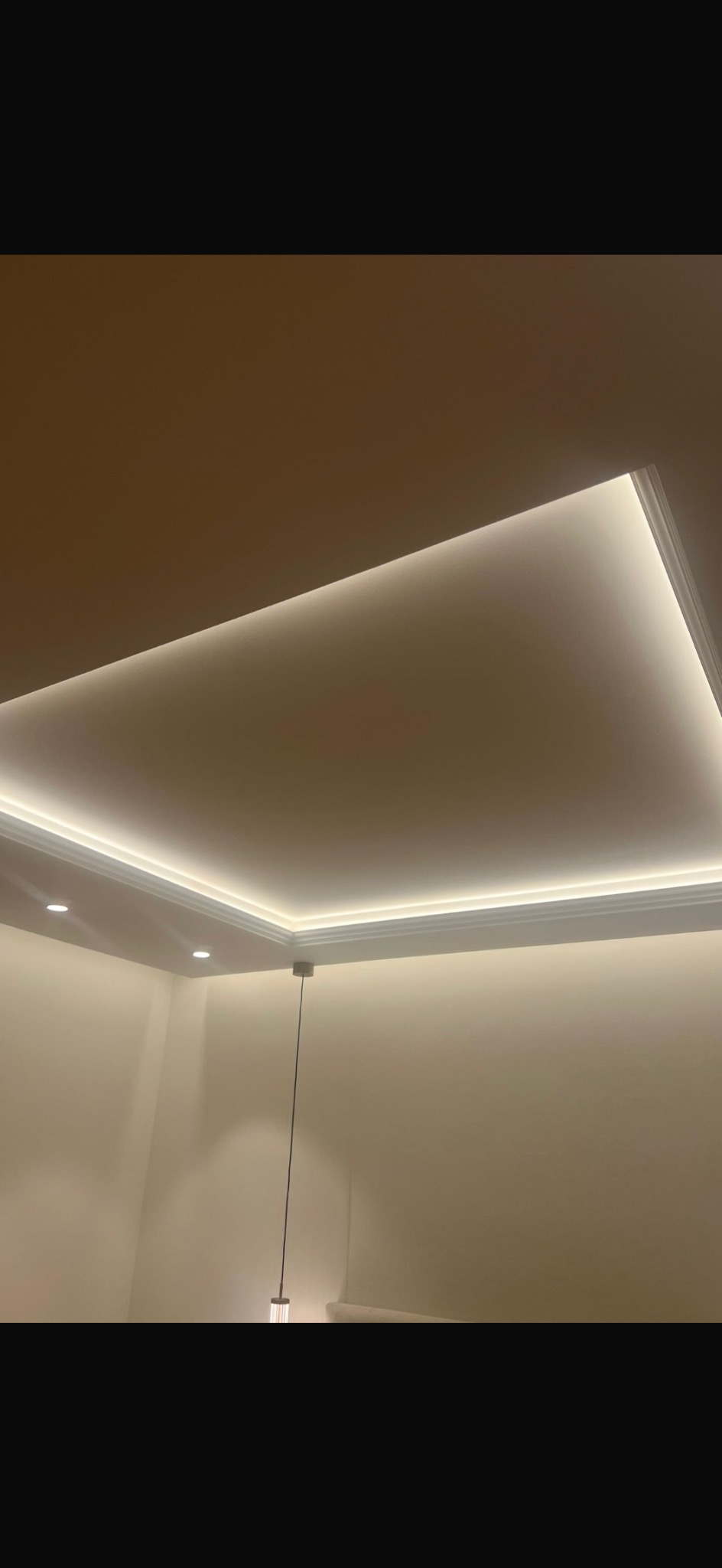 Sufit z dekoracyjnym oświetleniem LED wzdłuż krawędzi, z dodatkowymi punktowymi lampami. Nowoczesny design wnętrza z subtelnym, ciepłym światłem.