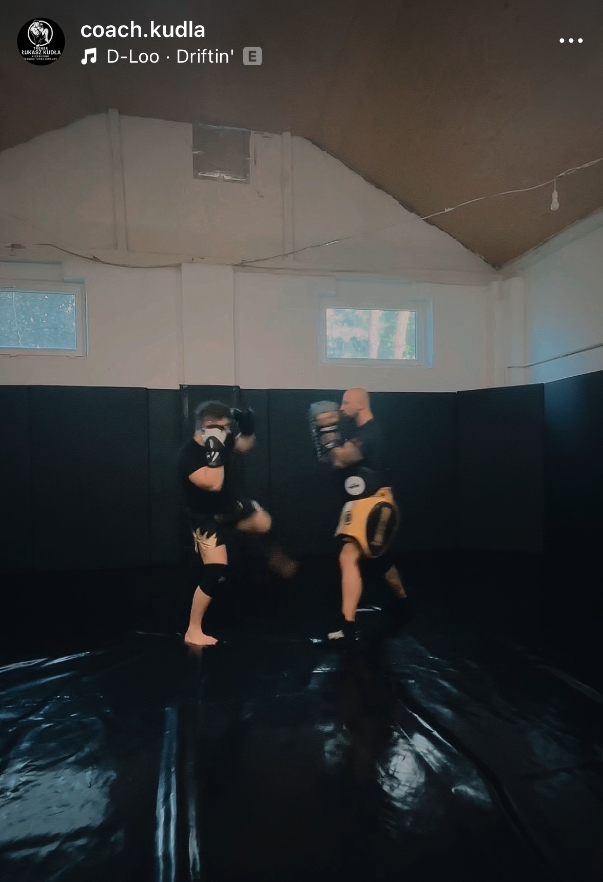 Trening sportów walki: uczeń w masce, ochraniaczach i rękawicach kopie, a trener z tarczą amortyzuje uderzenie. Akcja w sali treningowej.