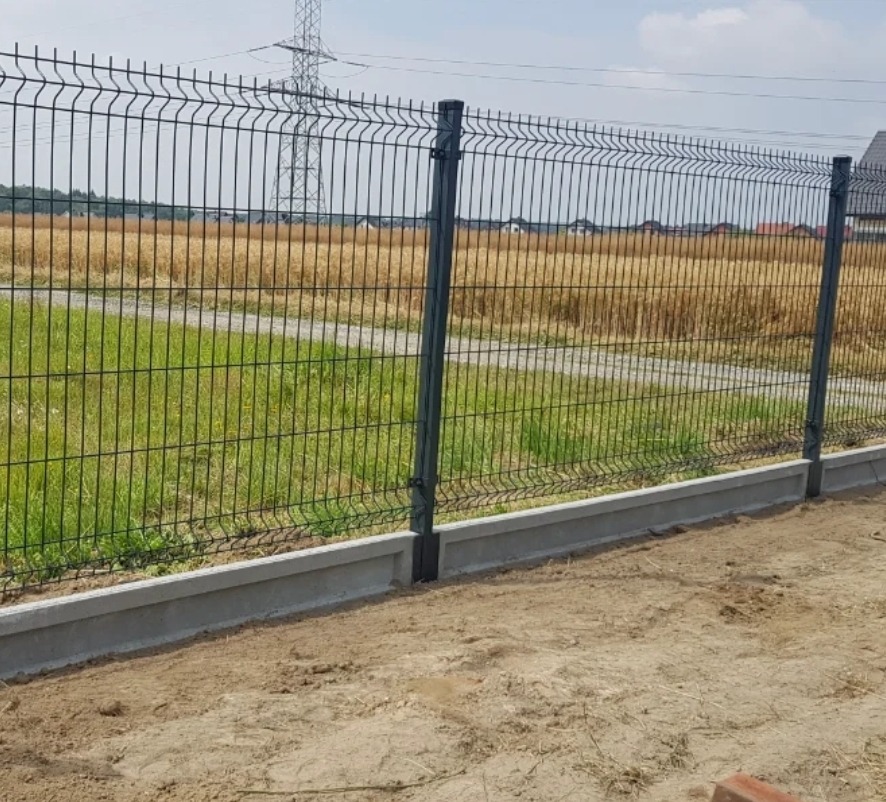 Nowoczesne ogrodzenie panelowe z podmurówką betonową na tle łąki i słupa energetycznego. Estetyczne zabezpieczenie posesji.