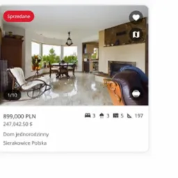 Jasne wnętrze domu z marmurową podłogą, widok na stół jadalny przy oknie i kominek. Na pierwszym planie fotel bujany i fragment skórzanego fotela.