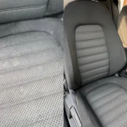 Tapicerka samochodowa przed i po praniu. Lewa strona fotela jest brudna, a prawa czysta. Widoczne detale struktury materiału.