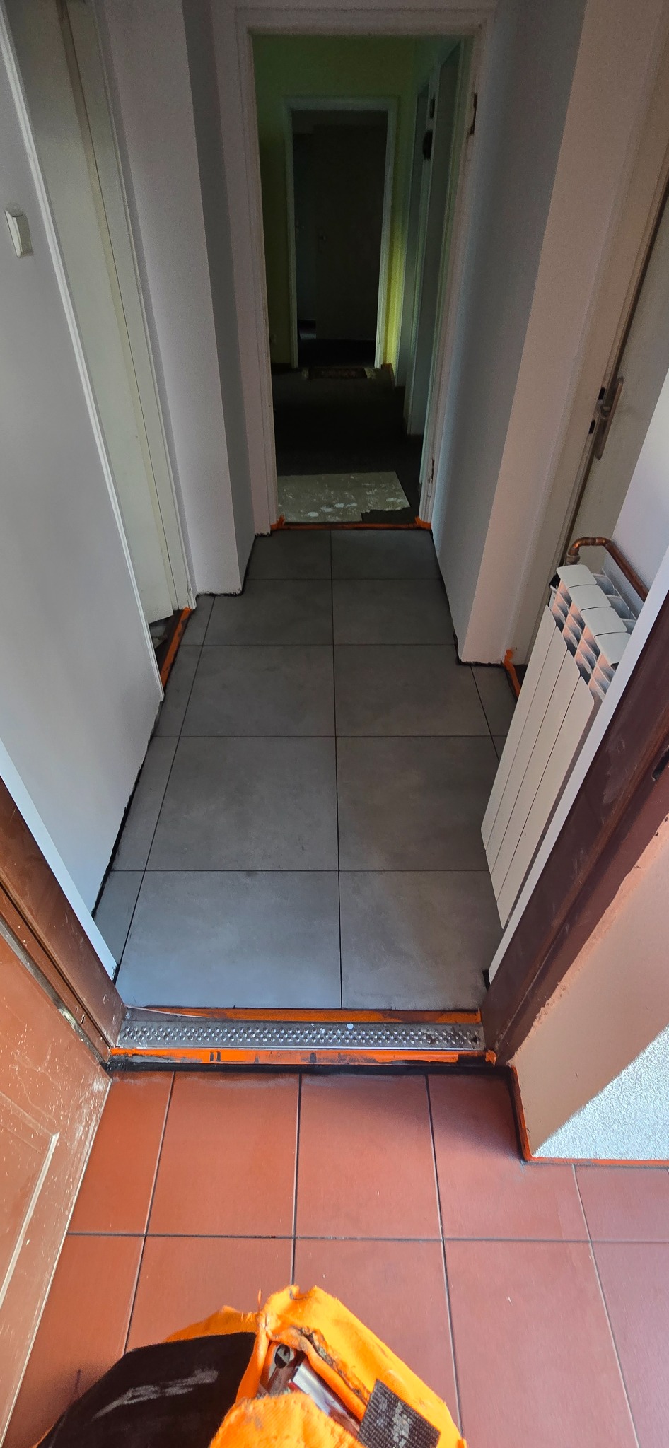 Korytarz po remoncie: szare płytki podłogowe, zabezpieczone folią malarską przy ścianach i drzwiach. W tle widoczne kolejne pomieszczenia.