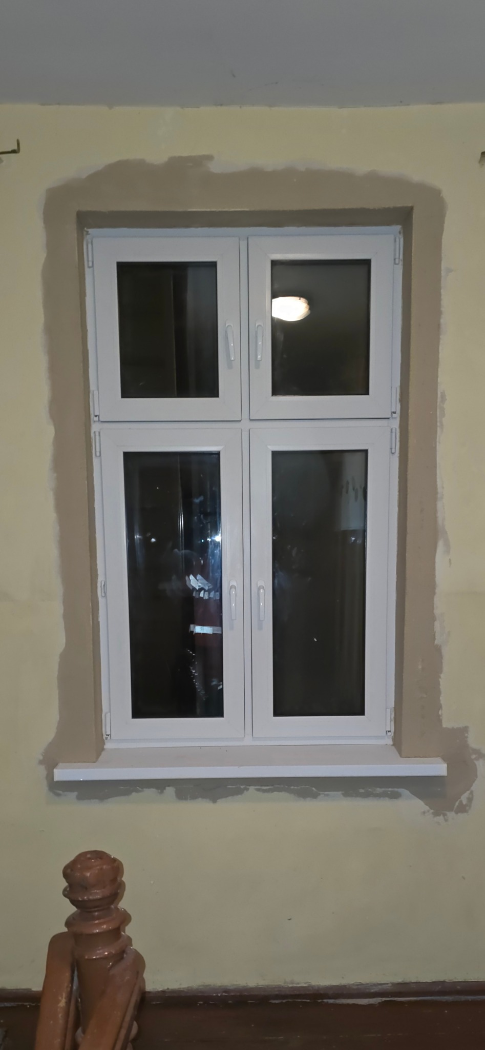 Białe okno PCV z czterema skrzydłami po montażu, widoczne ślady po gładzi na ścianie. Ujęcie z dołu, na pierwszym planie fragment balustrady.