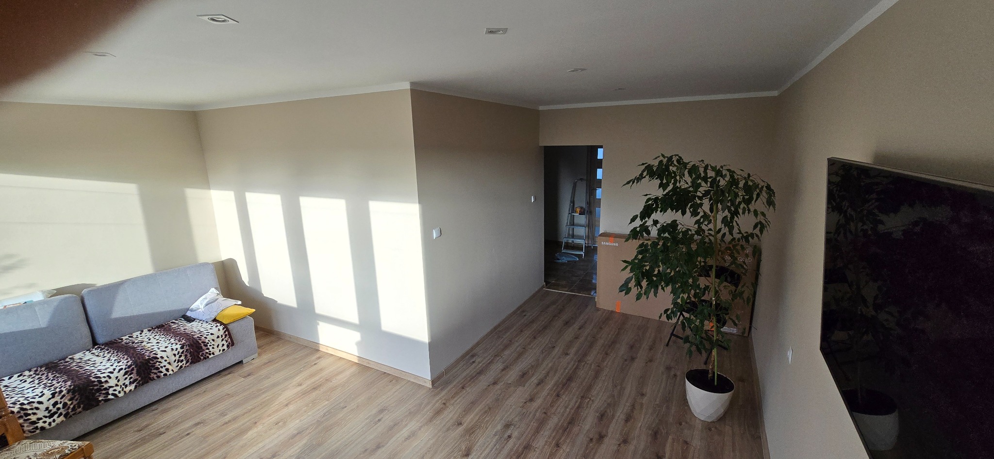 Jasne wnętrze po remoncie w Inowrocławiu: świeżo pomalowane ściany w odcieniach beżu, panele podłogowe, sofa i roślina doniczkowa. Widoczne światło słoneczne.