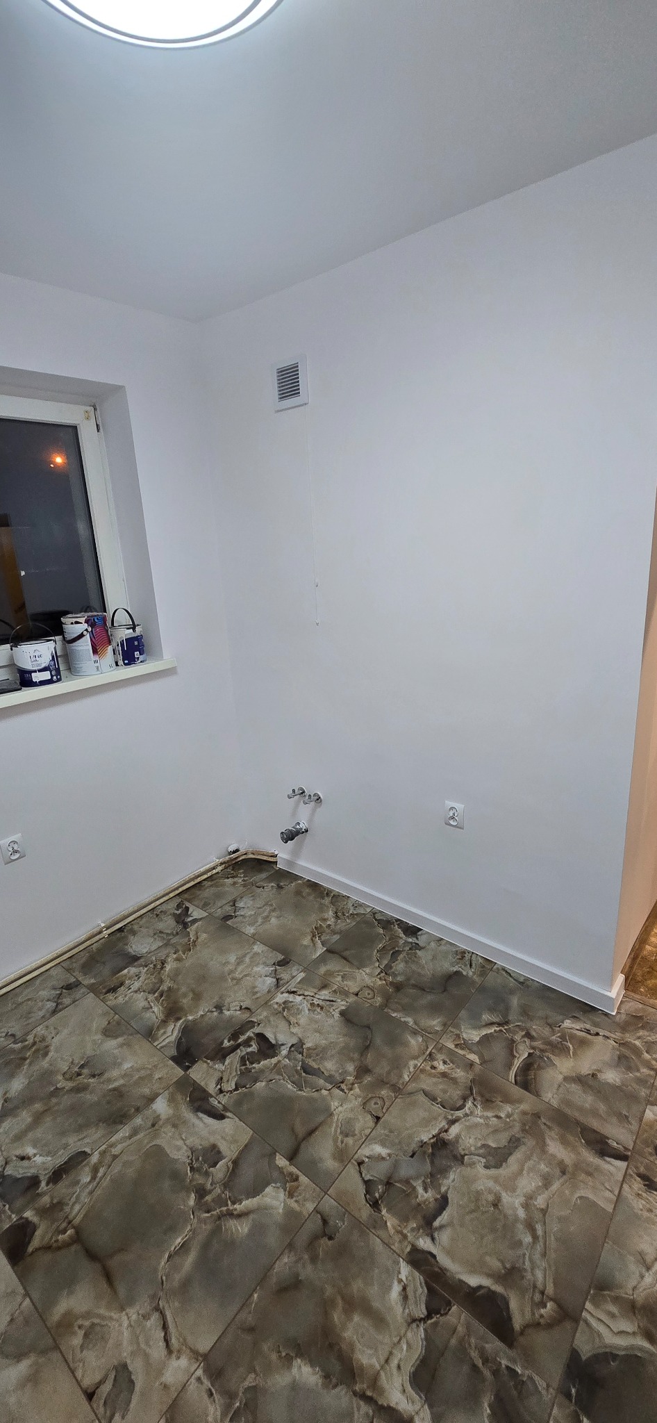 Wykończona łazienka z marmurową podłogą, białe ściany, okno z farbami. Widoczne przyłącza wodne. Nowoczesny design, jasne wnętrze, detale wykończeniowe.