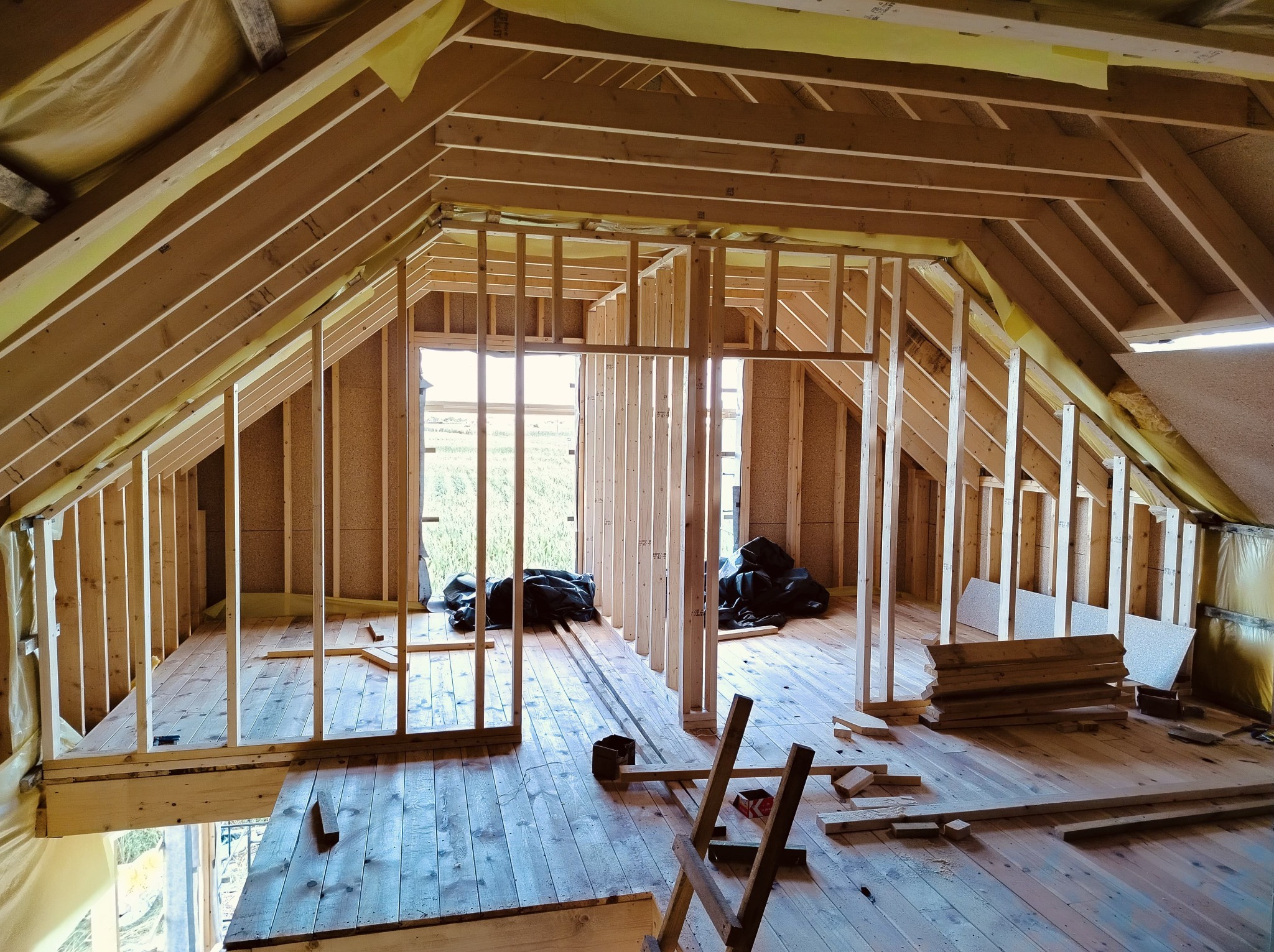 Wnętrze domu szkieletowego w trakcie budowy we Wrocławiu. Widoczne drewniane elementy konstrukcyjne, ściany w surowym stanie i przygotowane materiały budowlane.