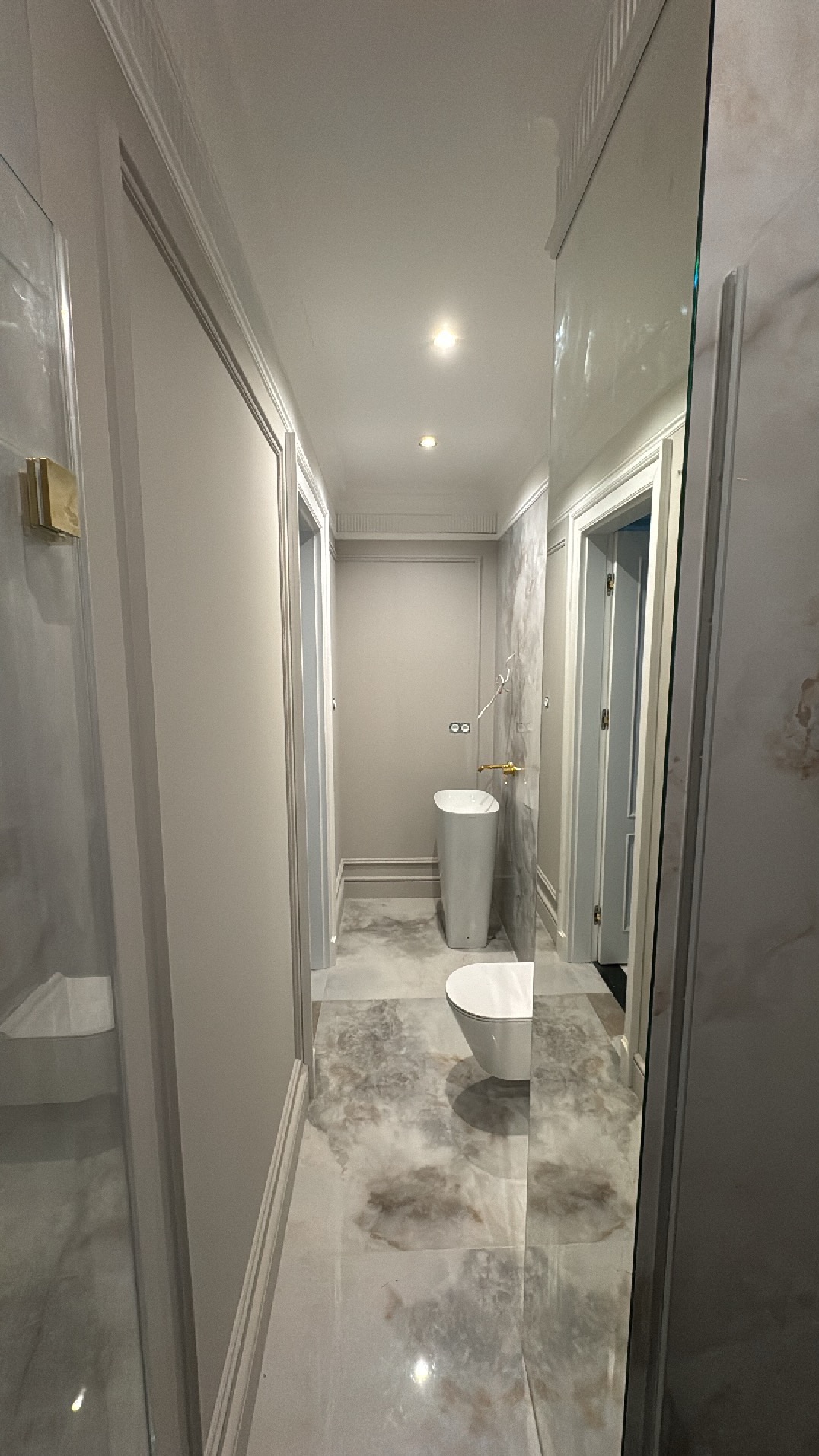 Elegancka łazienka po remoncie: marmurowe płytki podłogowe, umywalka kolumnowa i toaleta. Widok z perspektywy wejścia, z lustrem po prawej stronie.