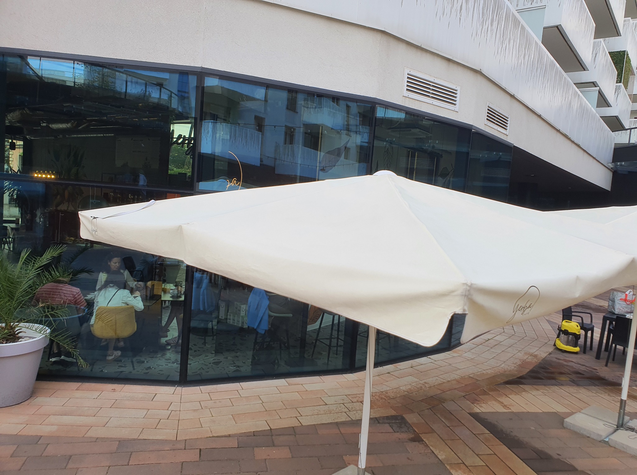 Mycie okien we Wrocławiu. Widok na umyte okna kawiarni spod parasola, z żółtym odkurzaczem do szyb w tle. Czyste szyby odbijają otoczenie.