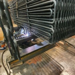 Well Welding Maciej Machulec - Proces łączenia metalowych rur przez spawanie. Widoczny spawacz w masce ochronnej, iskry i elementy konstrukcji. Ujęcie z bliska, oddające detale pracy.