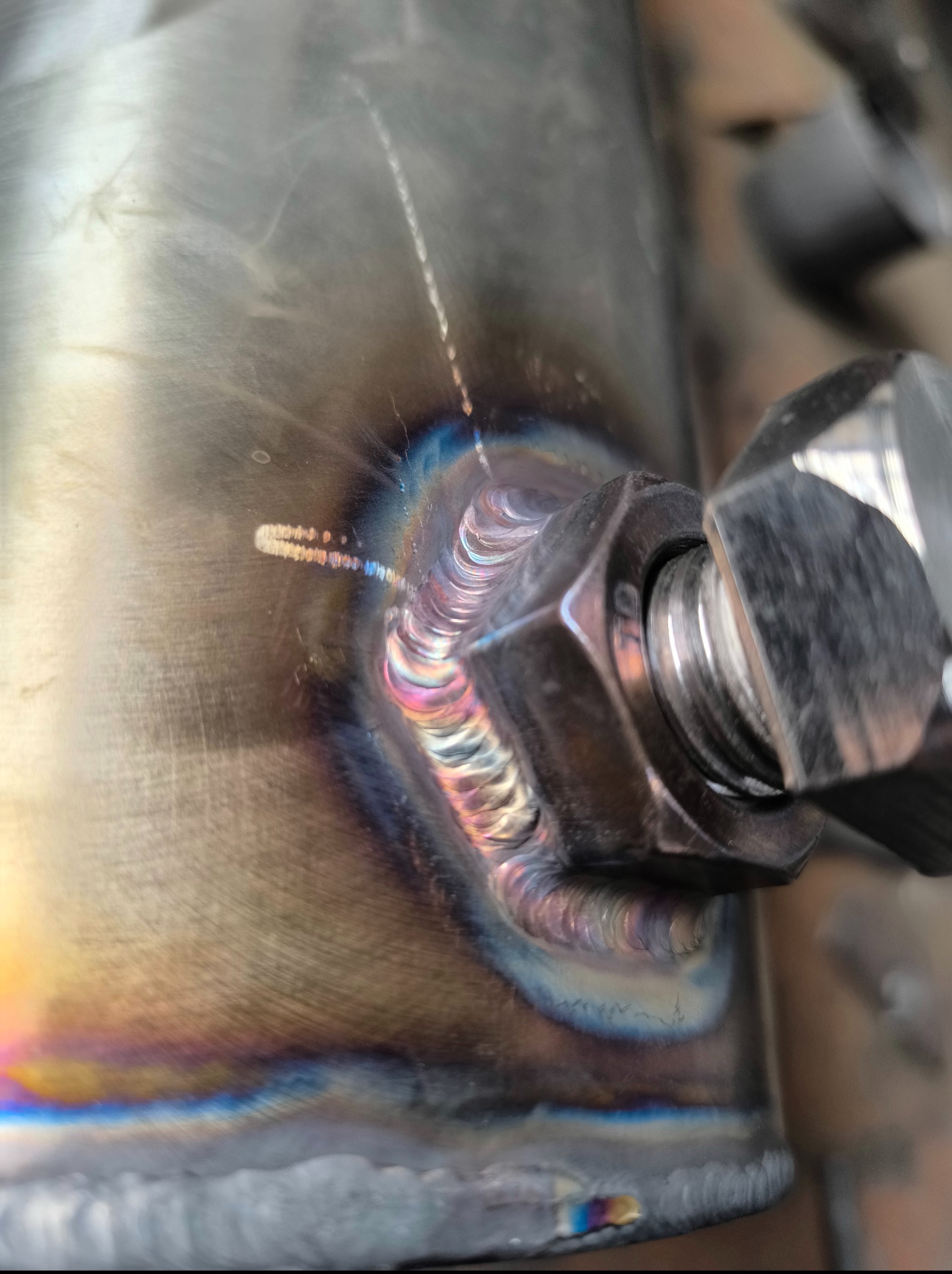 Zbliżenie na precyzyjne spawy łączące nakrętkę z metalową powierzchnią, ukazujące charakterystyczne, opalizujące zabarwienie termiczne.