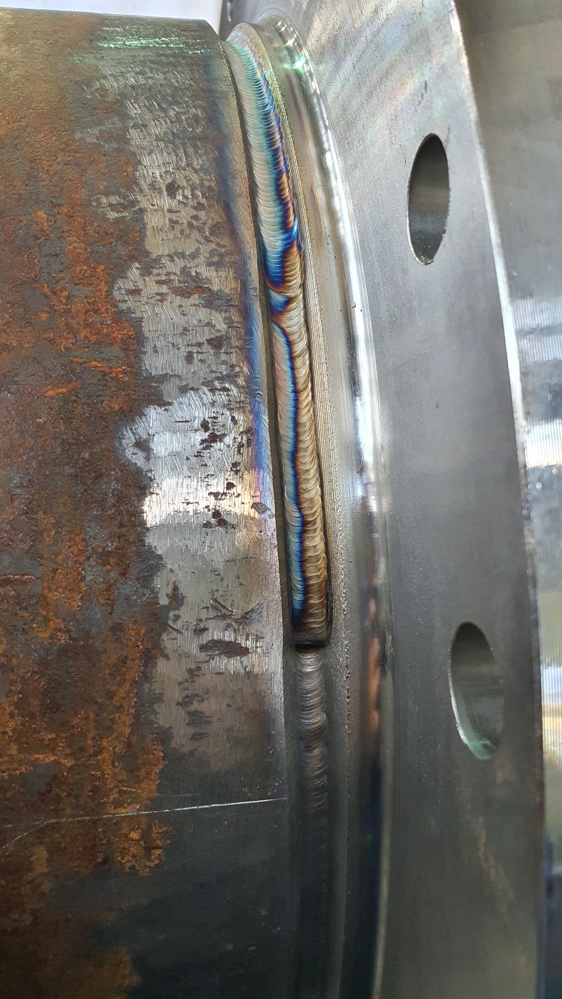 Spoina łącząca rurę z kołnierzem, widoczne charakterystyczne przebarwienia termiczne na spoinie. Obróbka metalu z bliska, detale wykonania.