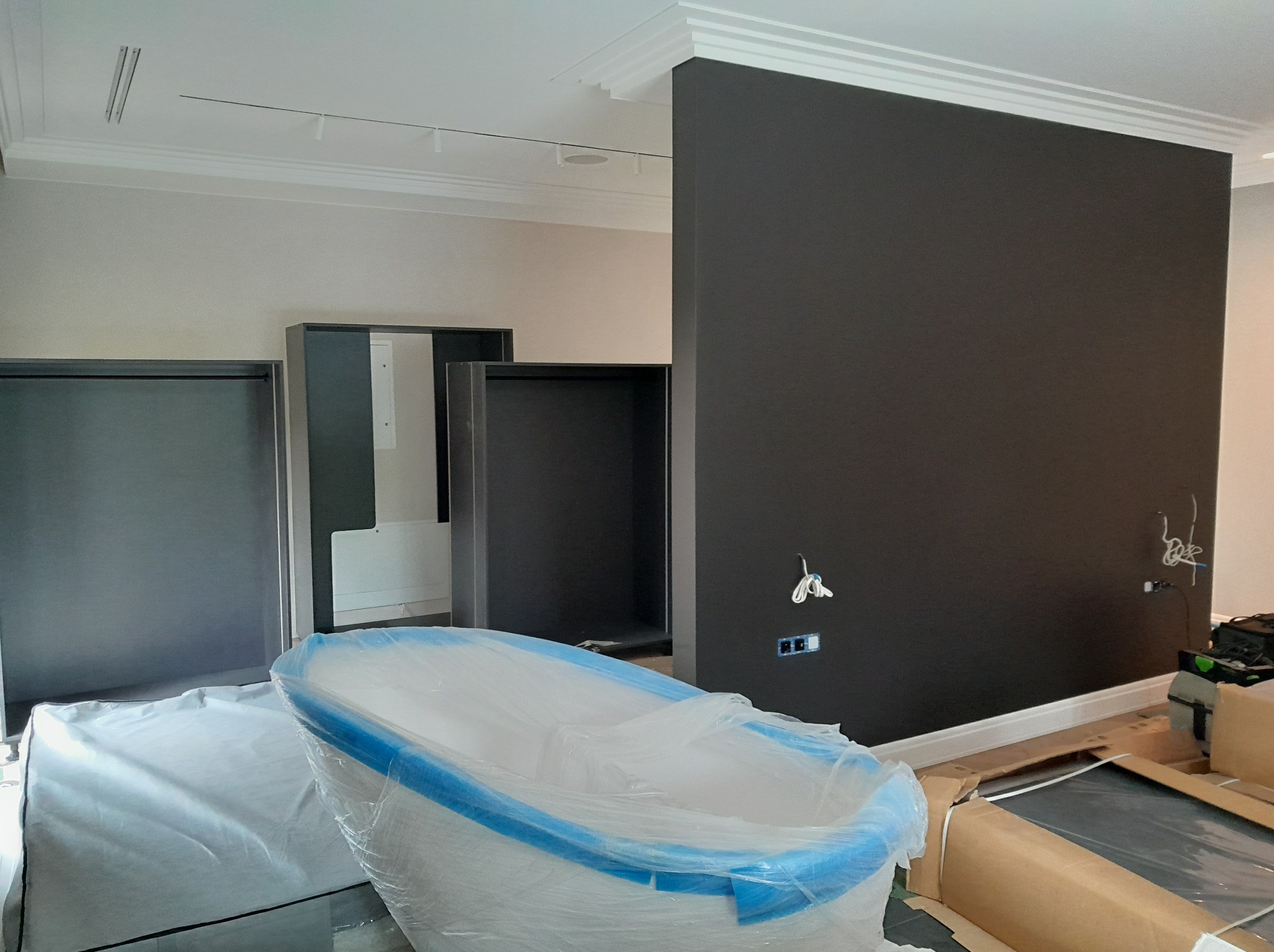 Montaż wyposażenia w łazience: wanna zabezpieczona folią, szafki bez frontów i ciemna ściana z instalacją elektryczną. W tle listwy dekoracyjne.