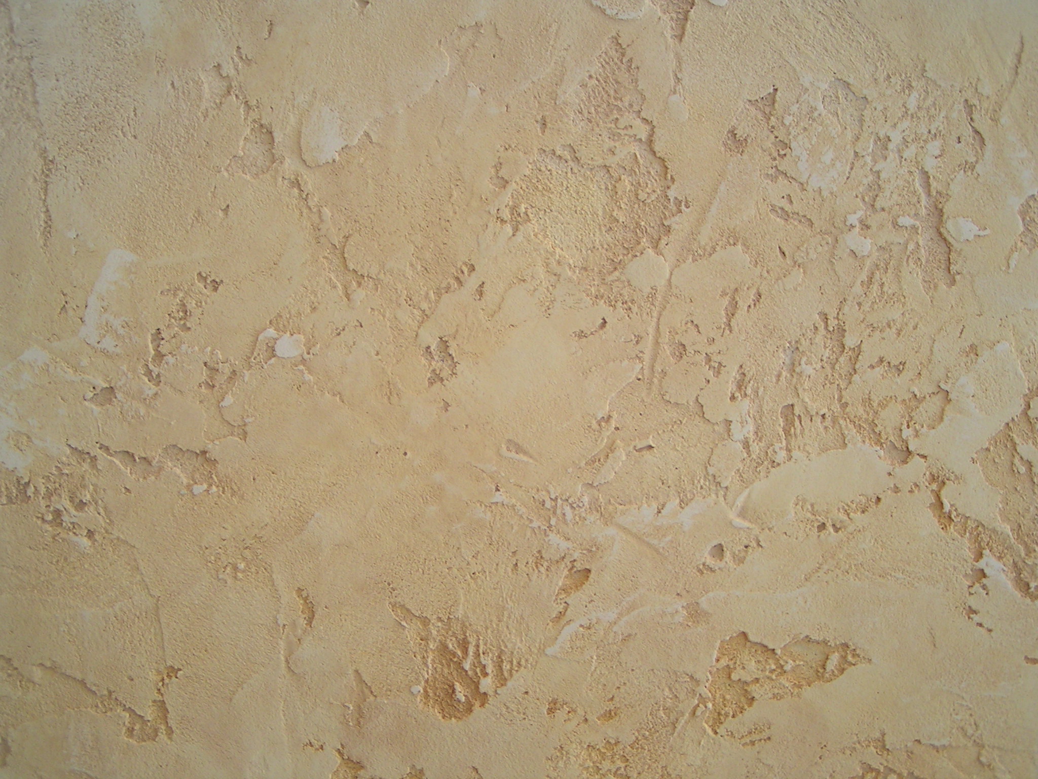 Beżowa ściana pokryta tynkiem strukturalnym o nieregularnej, chropowatej fakturze z widocznymi zagłębieniami i wypukłościami, imitująca stary tynk.