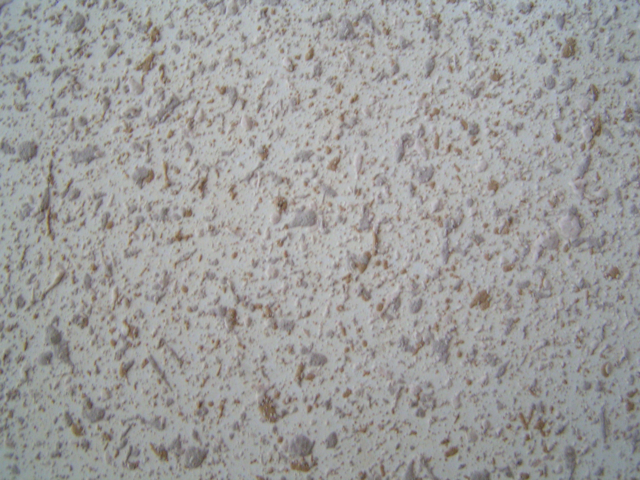 Jasna ściana pokryta natryskową fakturą z drobnymi, nieregularnymi wypukłościami w odcieniach brązu i szarości.