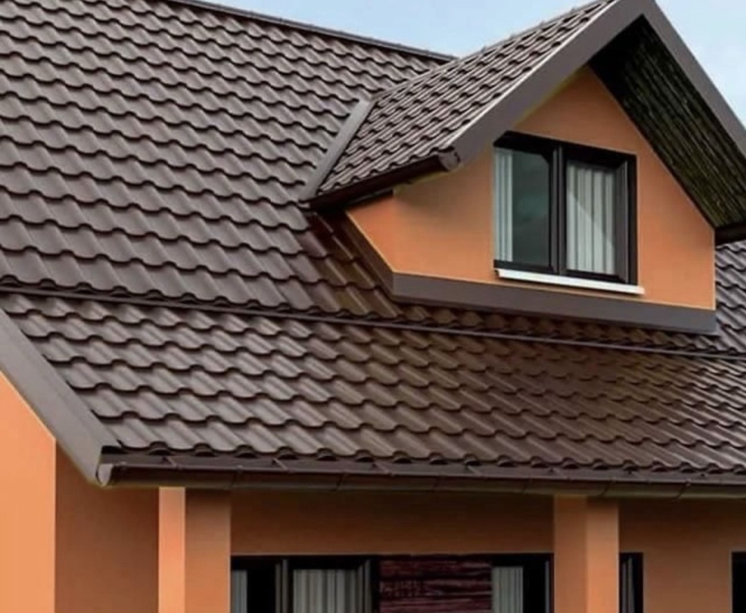 Dom z brązowym dachem z blachodachówki, okno dachowe z czarną ramą i brązowe rynny, pomarańczowa elewacja.