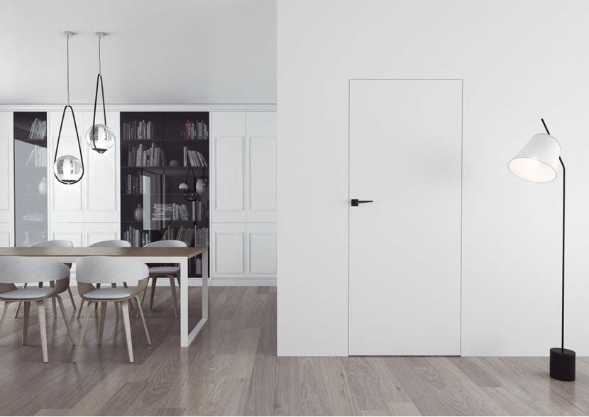 Minimalistyczne, białe drzwi wewnętrzne z czarną klamką, wkomponowane w ścianę, w jasnym wnętrzu z drewnianą podłogą i lampą podłogową.