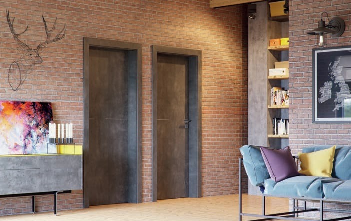 Dwa nowoczesne, szare drzwi wewnętrzne na tle ściany z czerwonej cegły. Po lewej stronie widoczny komoda z dekoracjami, a po prawej sofa i regał z książkami.