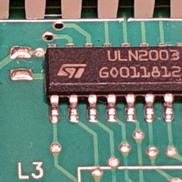 Alex Crisard - Zbliżenie na układ scalony ULN2003 ST na zielonej płytce drukowanej z widocznymi ścieżkami i punktami lutowniczymi. Widoczne oznaczenia i numer seryjny.