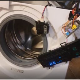 Alex Crisard - Otwarta pralka z widocznym bębnem i odłączonym panelem sterowania z podświetlonym wyświetlaczem, sugerująca naprawę lub serwis urządzenia.