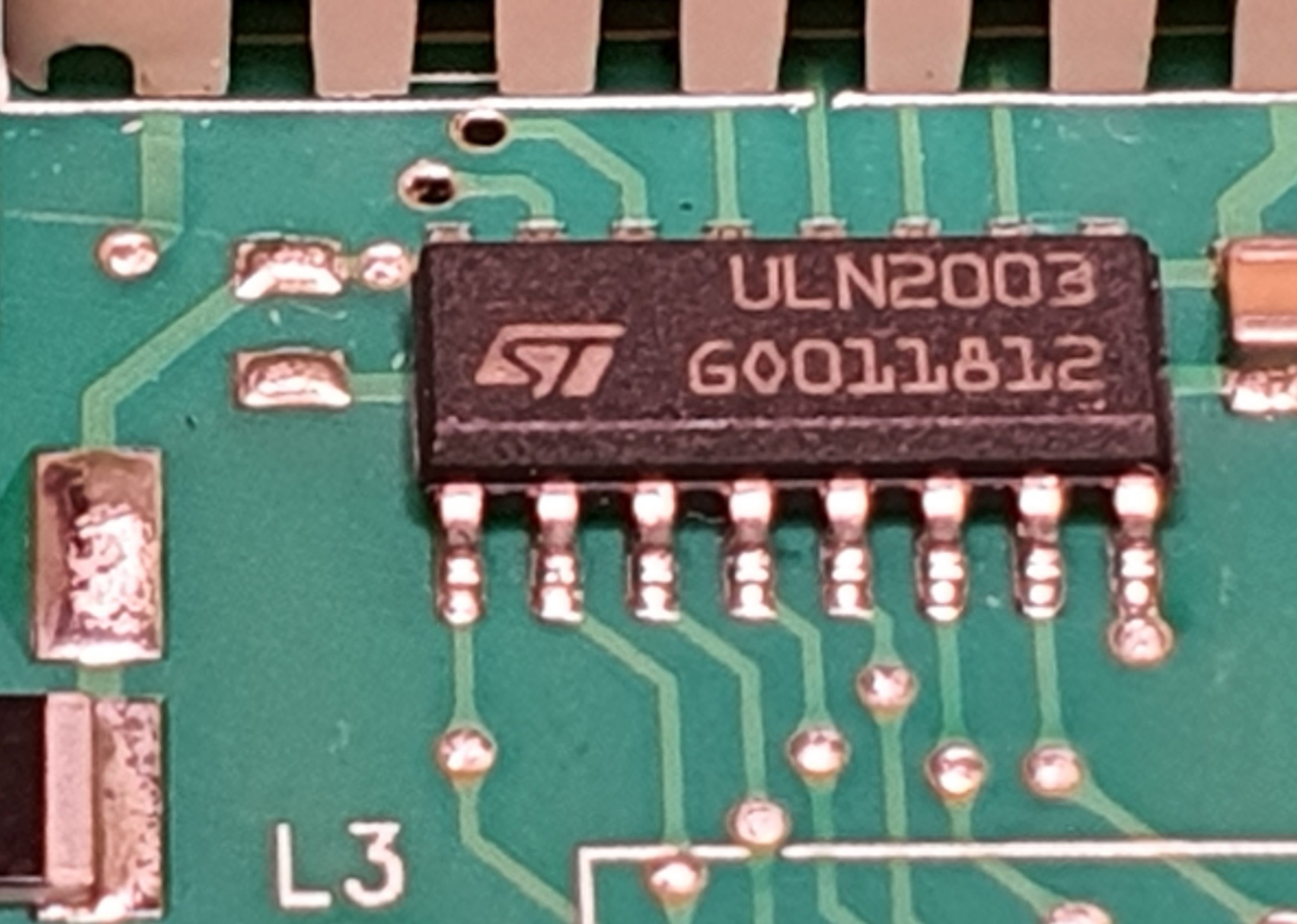 Zbliżenie na układ scalony ULN2003 ST na zielonej płytce drukowanej z widocznymi ścieżkami i punktami lutowniczymi. Widoczne oznaczenia i numer seryjny.