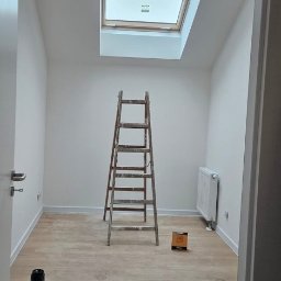eMBUD - Pokój po malowaniu z drewnianą drabiną, pudełkami po farbie i oknem dachowym. Podłoga wyłożona panelami. Białe ściany i listwy przypodłogowe.