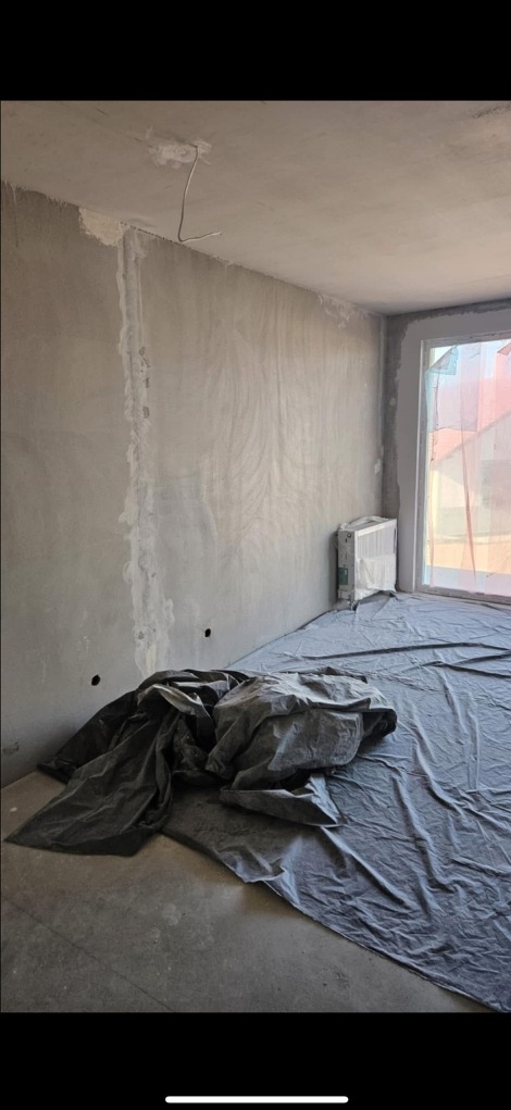 Surowe ściany w pokoju przygotowane do szpachlowania, zabezpieczone folią malarską na podłodze, widoczne ślady po instalacjach elektrycznych.