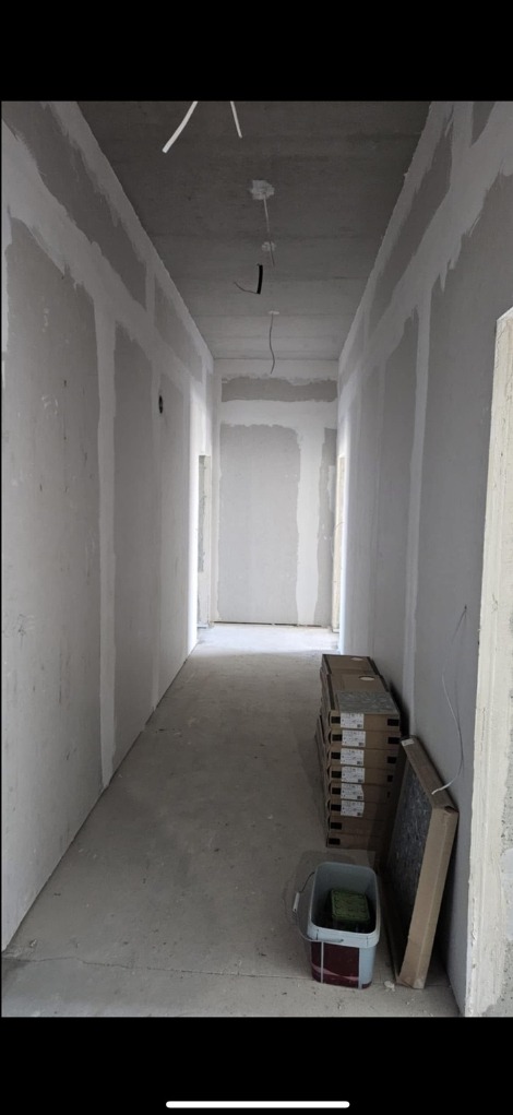 Korytarz w trakcie prac wykończeniowych: ściany z płyt gipsowo-kartonowych, widoczne łączenia, surowy beton, przygotowane materiały i narzędzia.