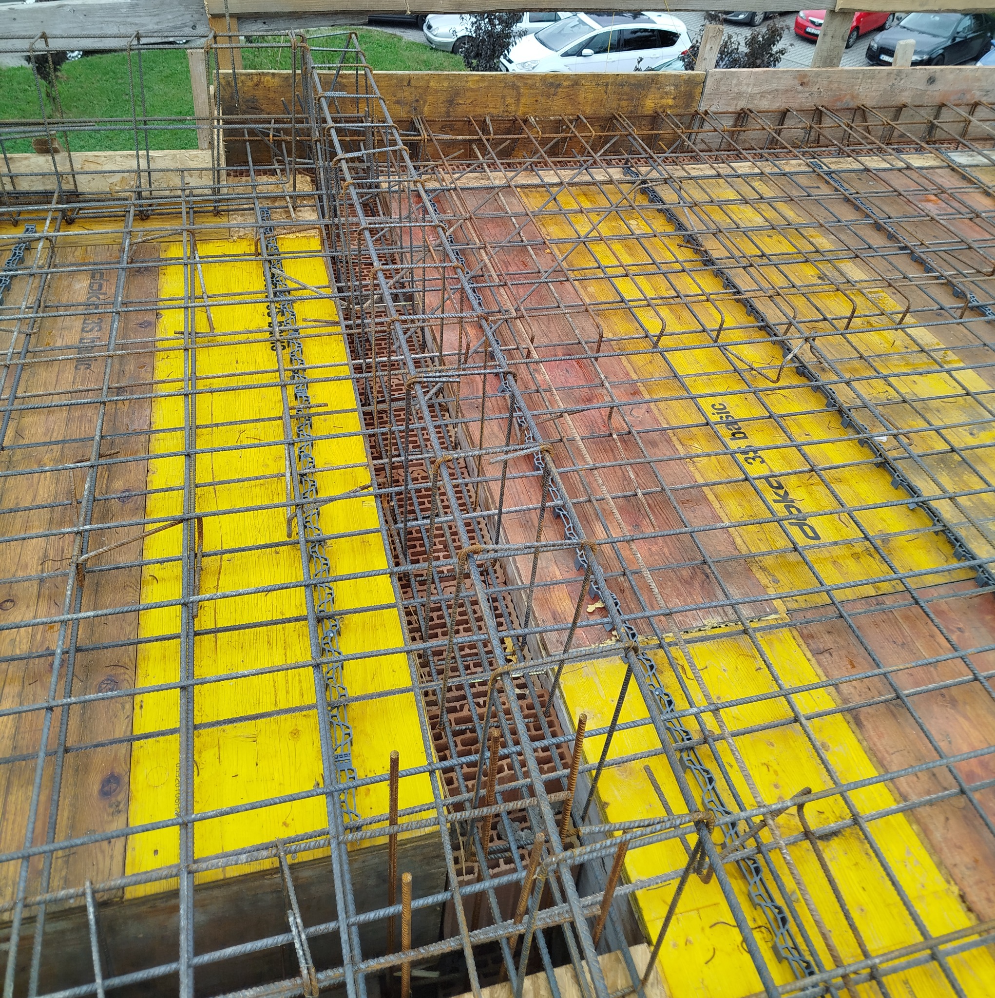 Zbrojenie stropu na żółtym szalunku, widok z góry. Stalowe pręty tworzą siatkę, przygotowane do zalania betonem. Elementy dystansowe z tworzywa.