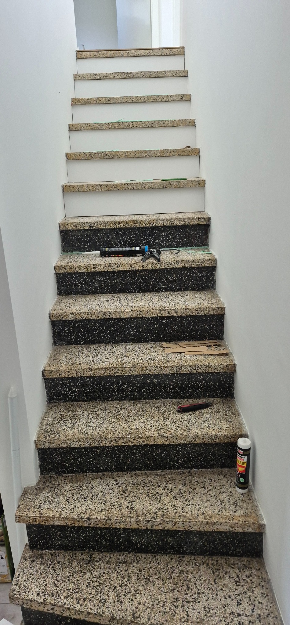 Schody z okładziną w trakcie montażu. Widoczny pistolet do kleju, docięte elementy i materiały montażowe. Część schodów wykończona białymi elementami.