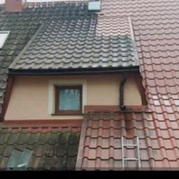 Częściowo umyty dach z dachówki ceramicznej, widoczna wyraźna różnica między czystą a zabrudzoną powierzchnią. Metalowa drabina oparta o dach.