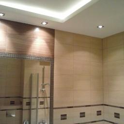 Usługi remontowe lux.house - Wykończona łazienka z beżowymi i brązowymi płytkami, oświetleniem punktowym w suficie i lustrem z widoczną armaturą.