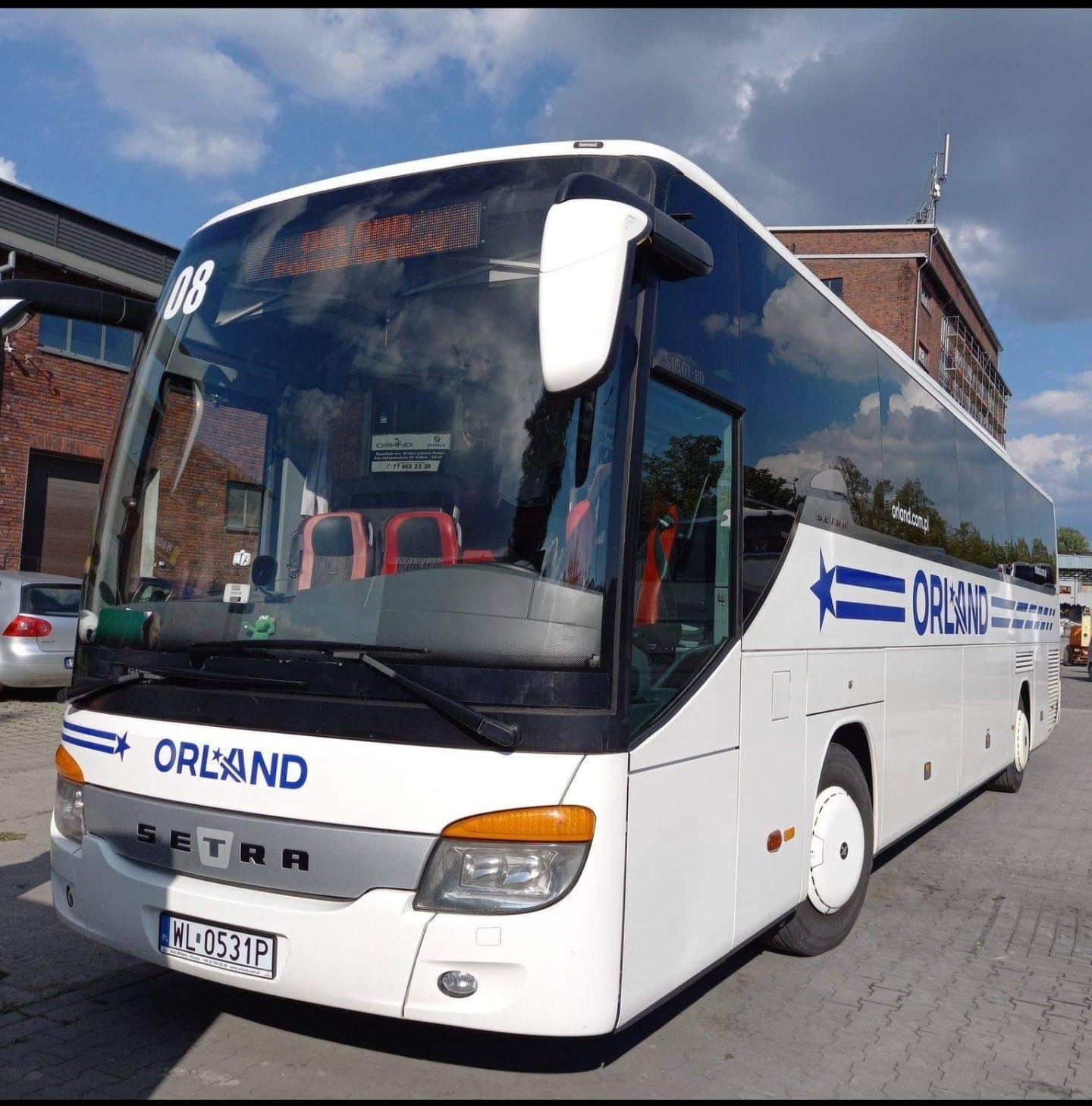 Biały autokar Setra z niebieskim logo Orland parkuje na tle ceglanego budynku i pochmurnego nieba. Widoczny numer '08' i tablica rejestracyjna WL-0531P.