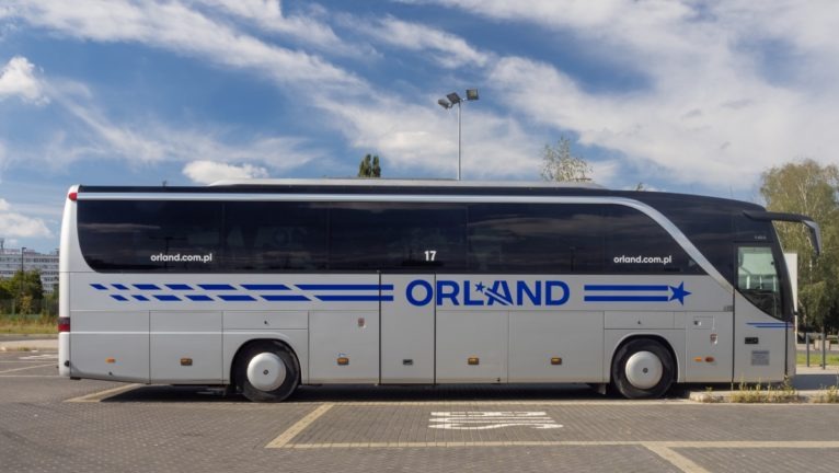 Autokar firmy Orland na parkingu w słoneczny dzień, widok z boku. Na pojeździe widoczny numer 17 i adres strony internetowej firmy.
