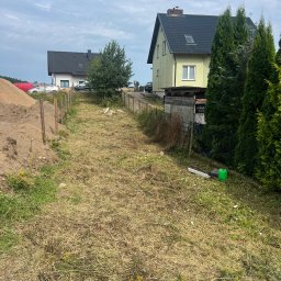 Usługi koparką DK - Działka z wytyczonym terenem pod budowę, widoczne domy w tle. Słupki ogrodzeniowe wzdłuż ścieżki, hałda ziemi po lewej stronie kadru.