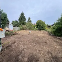 Przygotowany teren pod budowę w Kartuzach. W tle widoczny biały plastikowy krzesło. Ziemia wyrównana, świeżo przekopana, gotowa pod dalsze prace.