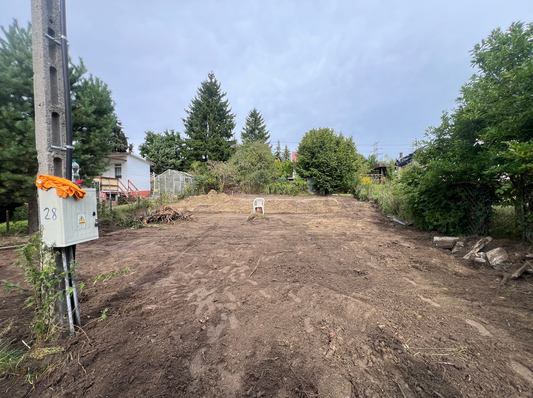 Przygotowany teren pod budowę w Kartuzach. W tle widoczny biały plastikowy krzesło. Ziemia wyrównana, świeżo przekopana, gotowa pod dalsze prace.