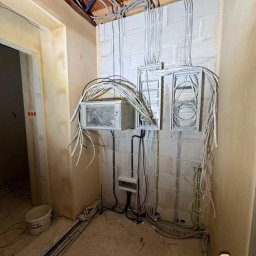GALTO Bartosz Gałkowski - Rozbudowa instalacji elektrycznej w pomieszczeniu przed wykończeniem: widoczne kable, puszki i rozdzielnice na ścianie z bloczków. Etap prac w surowym stanie.